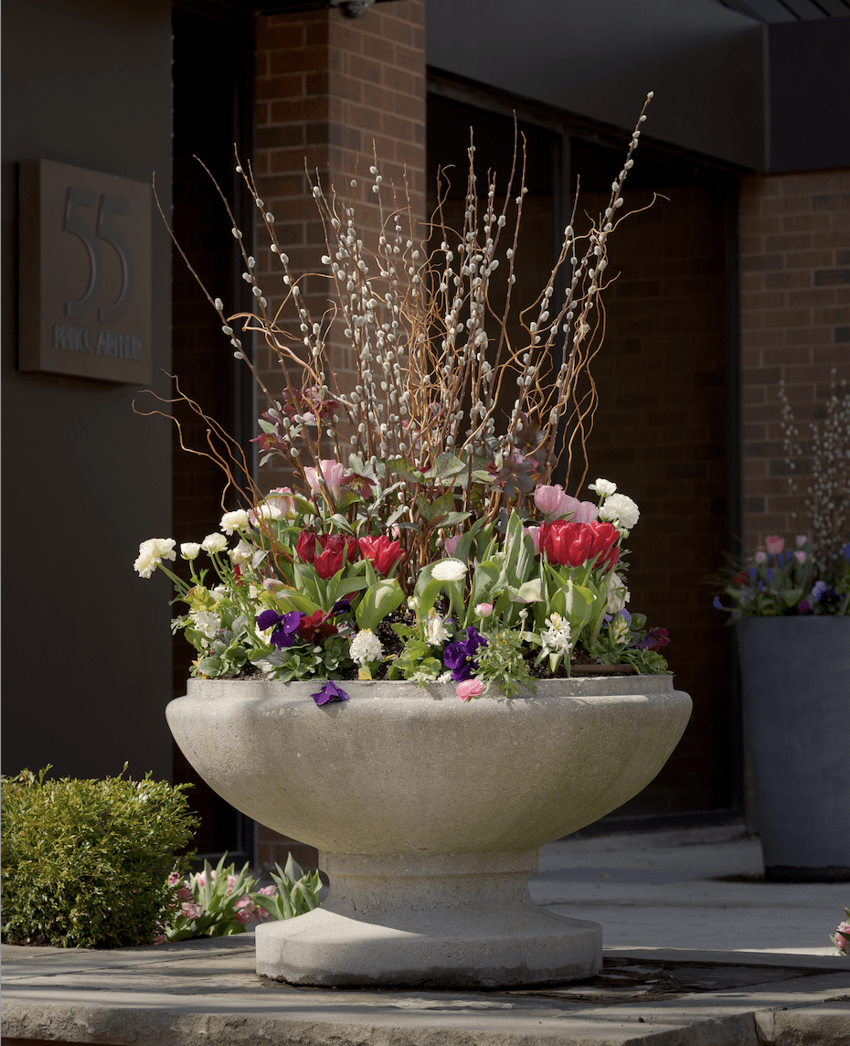 A decorative stone planter with colorful flowers and twigs sits outside a brick building, marked with the sign "55 Park Avenue."